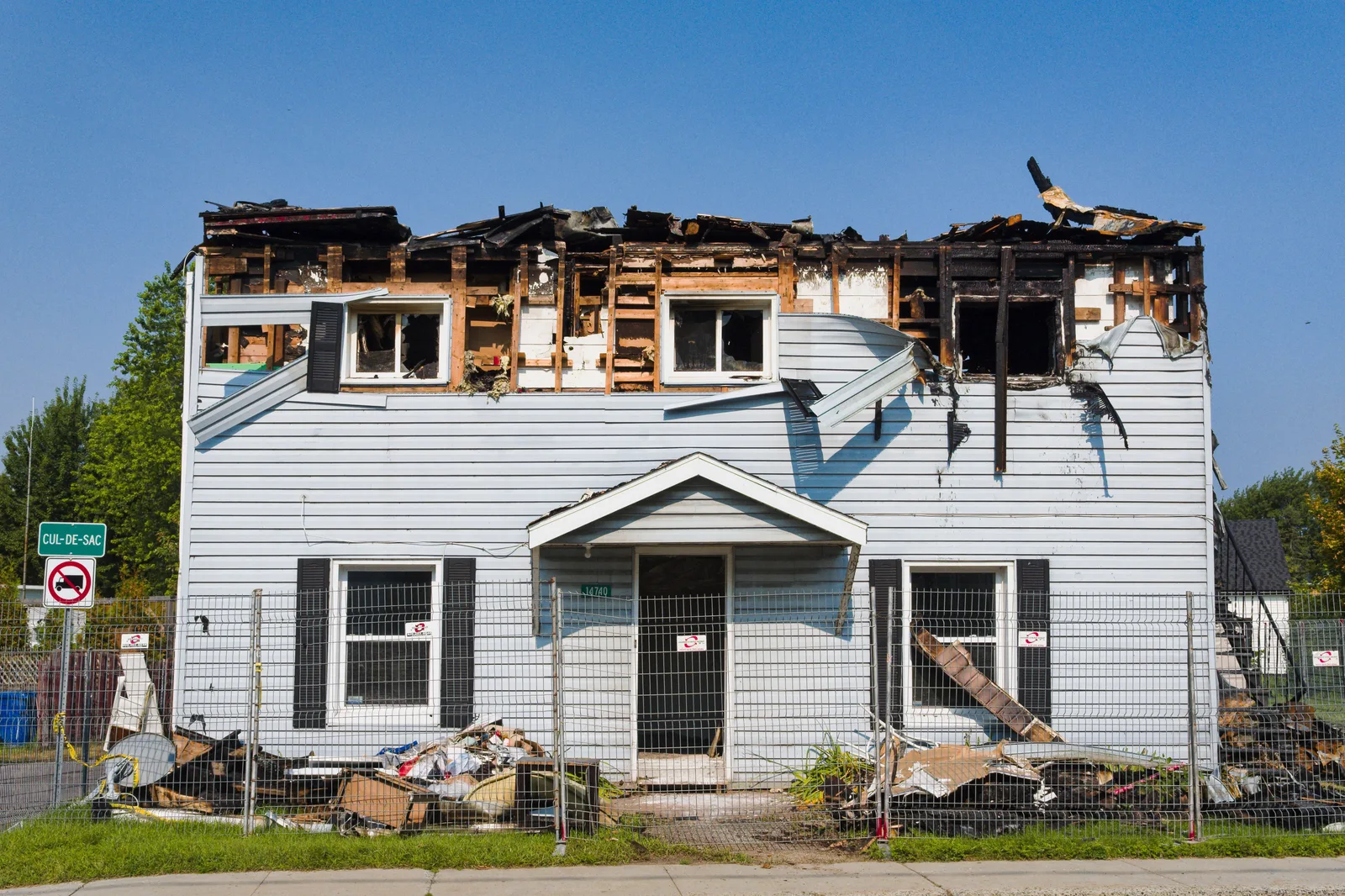 A damaged house with a burnt roof in Bécancour, Quebec, surrounded by a fence. Water damage restoration job costing: US labour rates vs Canadian provincial rates