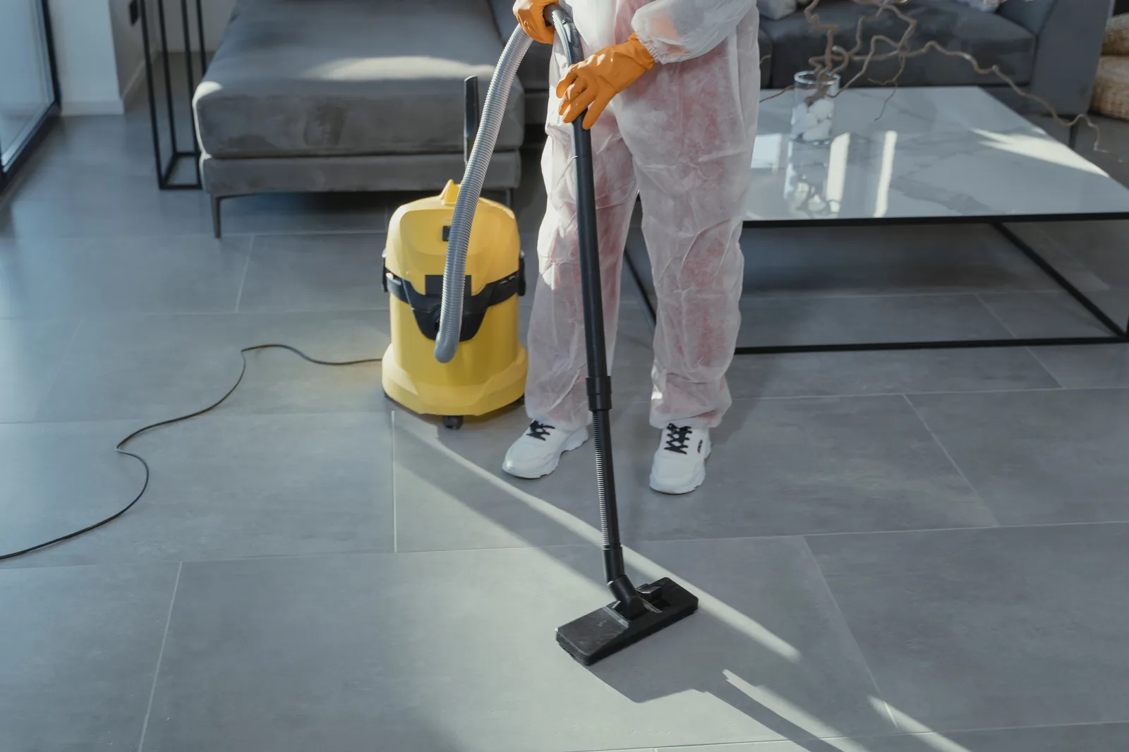 A professional cleaner in protective gear vacuuming the floor in a modern living room. The bookkeeping routine that keeps a water restoration business solvent, explained