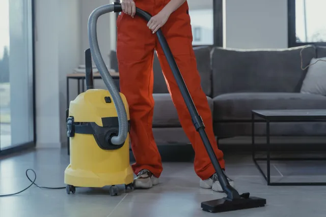 A professional cleaner in red coveralls vacuums a contemporary living room with a yellow vacuum cleaner. The real cost of insuring a water restoration business for 2027