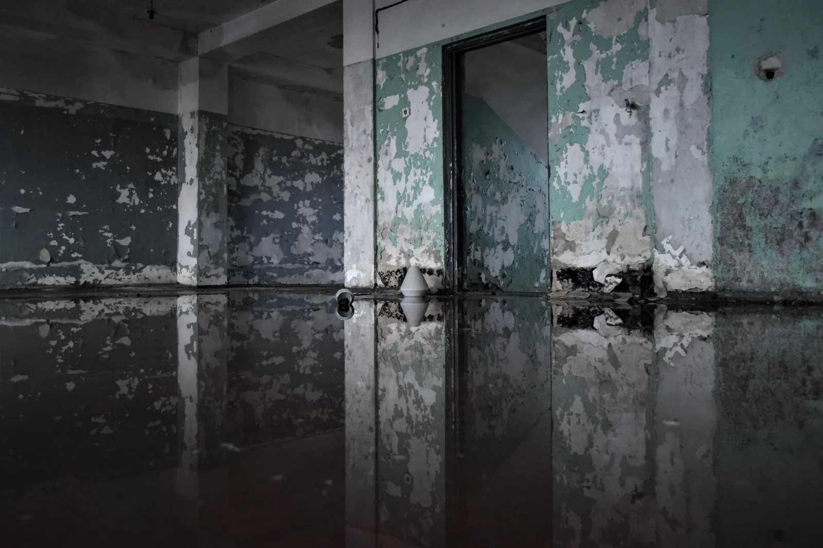 A decaying abandoned room with peeling paint and flooded floor, creating a reflection effect. How do Canadian restoration firms price jobs under provincial labour rates?
